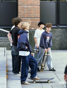 four boys are standing on the sidewalk with their skateboards and one boy is holding onto his skateboard