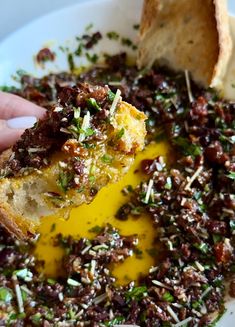 a plate with bread, olives and other toppings on it is being held up by a hand