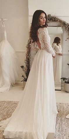 a woman standing in front of a mirror wearing a wedding dress with long sleeves and open back