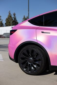 a pink car parked in a parking lot next to another car with black rims