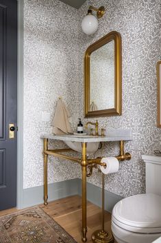 a white toilet sitting next to a bathroom sink under a golden framed mirror on a wall