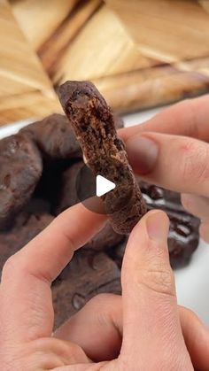 a person holding a piece of chocolate in their hand and some cookies on the other side