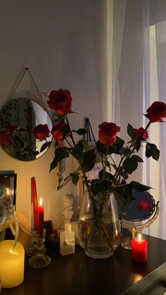 red roses in vases and candles on a table next to a mirror with a candle