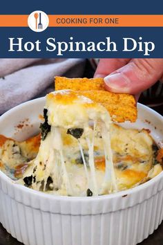 a person dipping cheese into a casserole dish with spinach dip on top