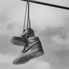 a pair of shoes hanging from a wire with cloudy skies in the backgroud