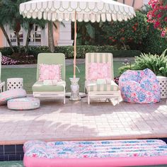 some lawn chairs and an umbrella by the pool in front of a house with pink flowers