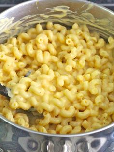 macaroni and cheese is being cooked in a pot on the stove with a spoon