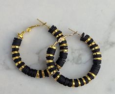 two pairs of black and gold hoop earrings on a marble countertop, with the top beaded in gold