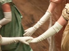 two women wearing white gloves and green dresses, one holding her hand up to the other