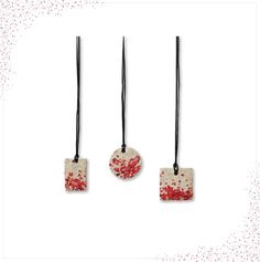 three square pendants with red and white designs hanging from black cords on a white background