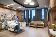 a hospital room with a bed, couch and chair next to large windows overlooking the city