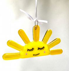 a yellow plastic sun ornament hanging from a white string with eyes drawn on it