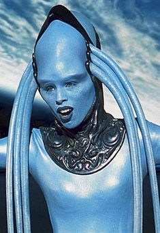 a woman with long hair and blue skin is wearing futuristic garb while looking at the camera