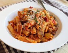 a white plate topped with pasta and meat covered in sauce on top of a checkered table cloth