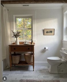 a white toilet sitting next to a window in a bathroom under a wooden beam with two baskets on top of it