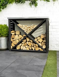 a firewood rack with logs in it on the ground next to a potted plant