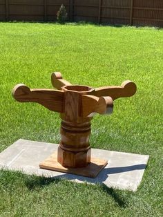 a wooden sculpture sitting on top of a cement slab in the grass next to a fence