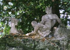 three statues sitting next to each other on top of a stone wall in front of trees