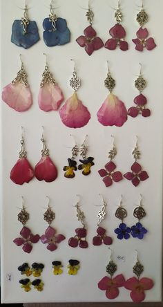 several pairs of earrings hanging from hooks on a white board with flowers and butterflies attached to them