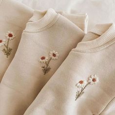 three white sweaters with daisies embroidered on them