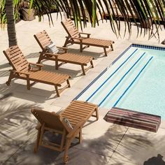 an empty swimming pool with lounge chairs and a table next to it, surrounded by palm trees