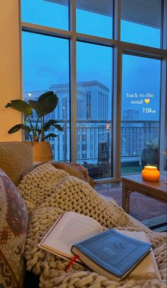 a living room filled with lots of furniture next to large windows and a book on the couch