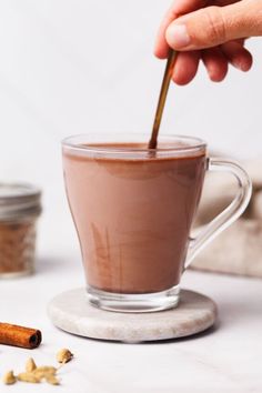 a person is holding a spoon in a cup of hot chocolate with cinnamons on the side