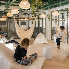 two women sitting on bean bags in an office with laptops and hammocks hanging from the ceiling