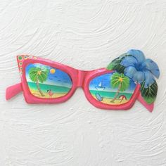 a pair of pink sunglasses with blue flowers on the side and palm trees reflected in them