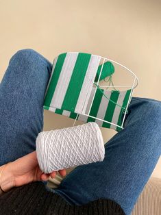 a person sitting on a couch holding a roll of yarn in front of a green and white striped basket