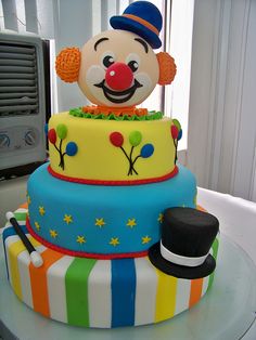 there is a multi layer cake decorated with a clown face and top hat on the table