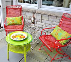 two red chairs and a yellow table with plates on it in front of a brick wall