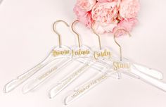 three clear hangers with gold lettering on them next to pink carnations and peonie