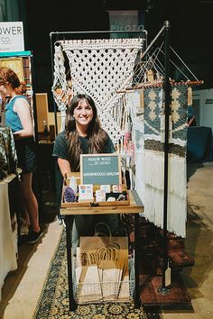 a woman standing in front of a table with some items on it at an art show