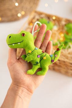 a hand holding a small green stuffed toy with lights on it's head and tail