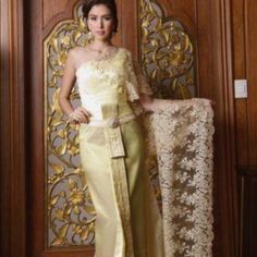 a woman standing in front of a wooden door wearing a white and gold dress with lace on it