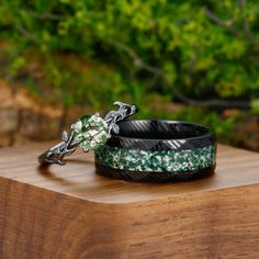 two bracelets sitting on top of a wooden table in front of some trees and bushes