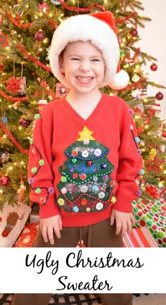 a young boy standing in front of a christmas tree wearing a red sweater and santa hat