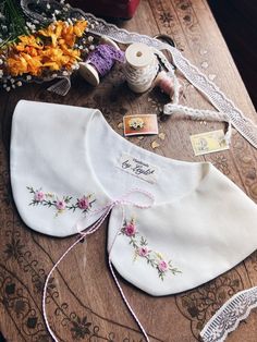 two white shirts with flowers on them sitting on a table next to some thread and spools