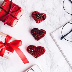 three red beaded hearts sitting on top of a table next to a pair of glasses