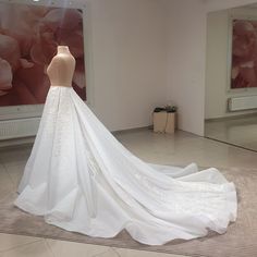 a white wedding dress on display in a room with large floral paintings behind it and a mannequin