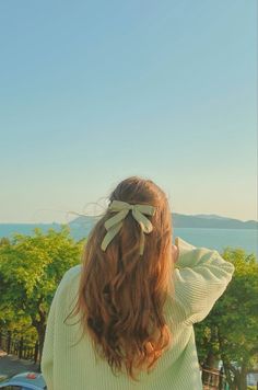 a woman with long hair wearing a bow in her hair looking out at the ocean