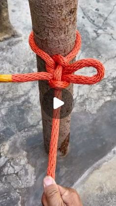 a person holding a rope attached to a pole with an orange knot around it and two yellow sticks sticking out of the top