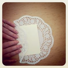 a hand holding a piece of paper on top of a doily covered wooden table