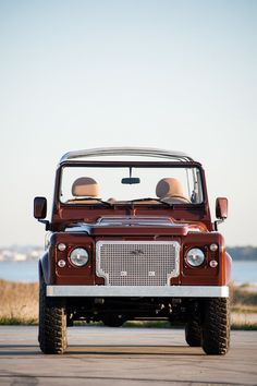 an old red jeep is parked by the water