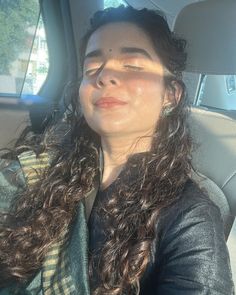 a woman sitting in the back seat of a car with her eyes closed and long curly hair