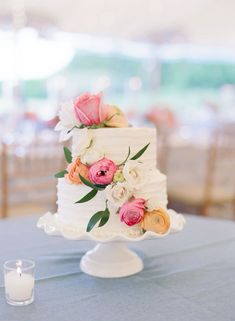 a white wedding cake with pink and orange flowers on it sitting on top of a blue table cloth