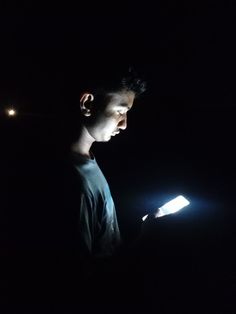 a man standing in the dark holding a cell phone and looking at it with light shining on his face