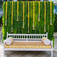 a white bench sitting in front of a green wall with yellow flowers hanging from it