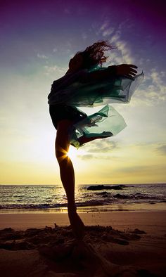 a woman is standing on the beach with her arms in the air while she's holding